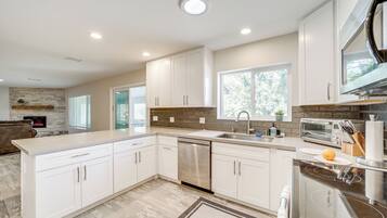 A modern kitchen with white cabinetry, a stainless steel dishwasher, a built-in oven, and a window providing natural light.