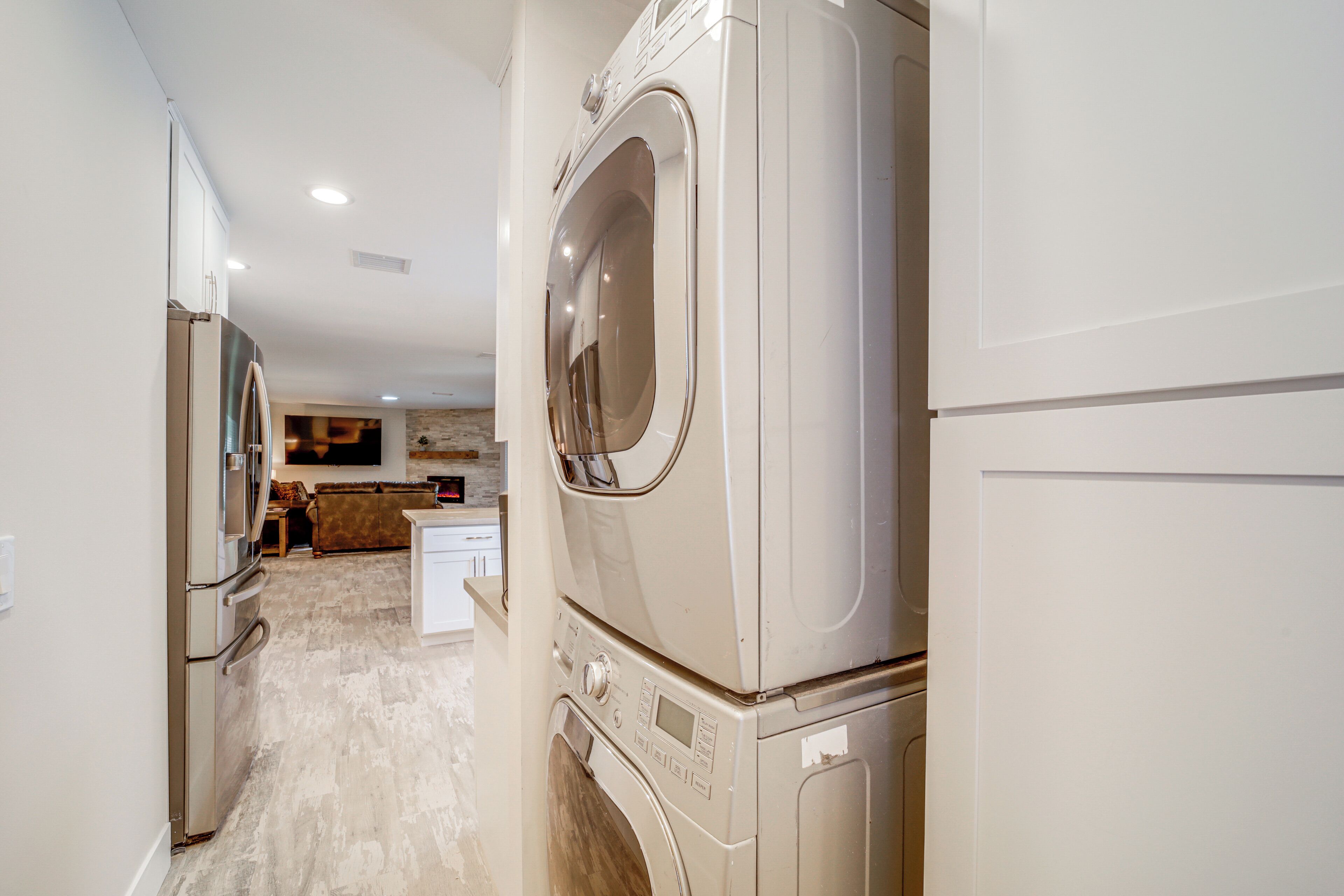 Une buanderie avec des lave-linge et des sèche-linge superposés, un réfrigérateur et un coin cuisine à l’arrière-plan.
