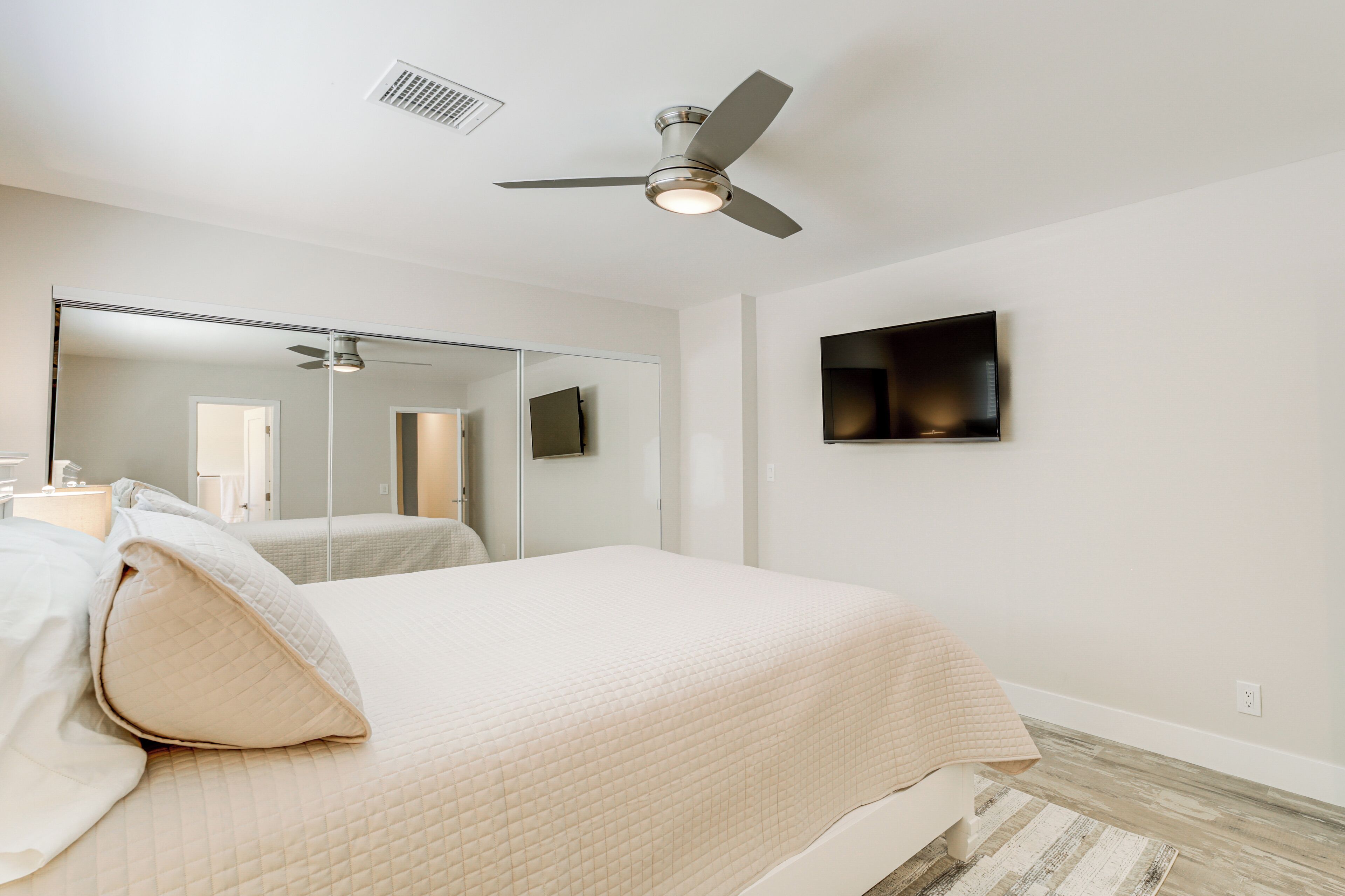 Un dormitorio con una cama, ventilador de techo, televisor y espejo.
