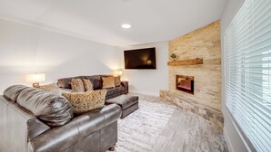 A modern living room with a leather sofa, a flat-screen TV mounted on the wall, and a fireplace.