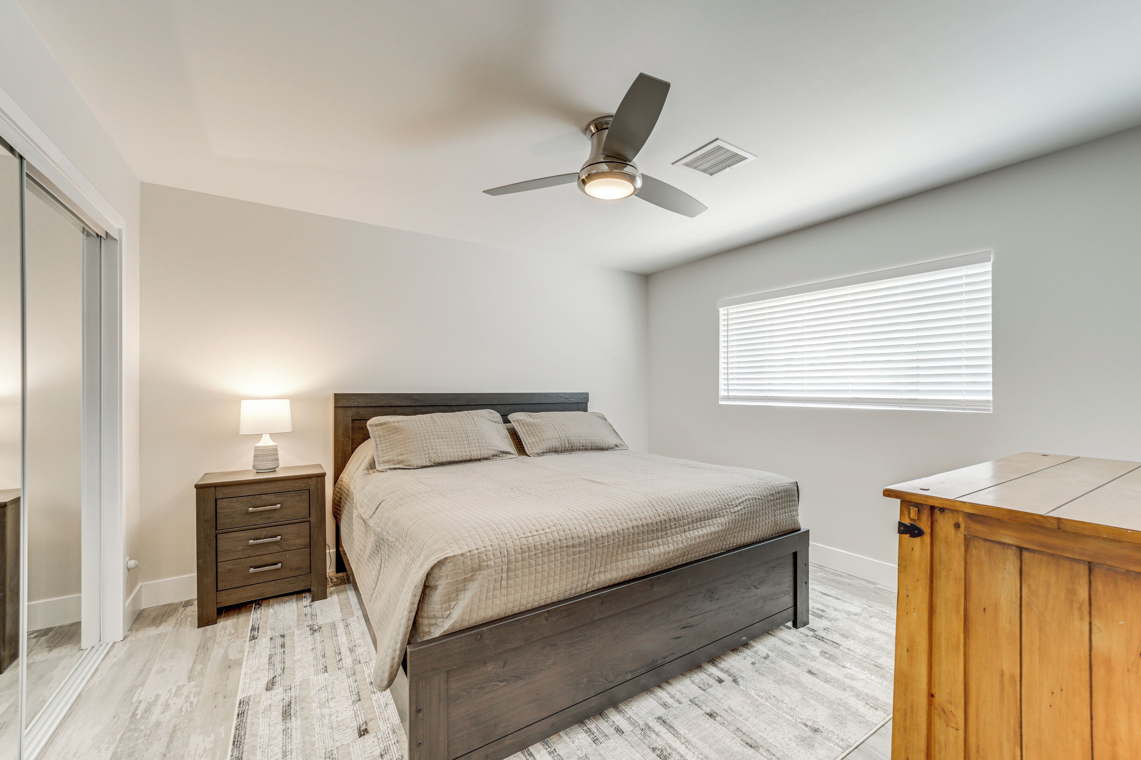 A bedroom with a bed, nightstand, lamp, ceiling fan, and a window with blinds.