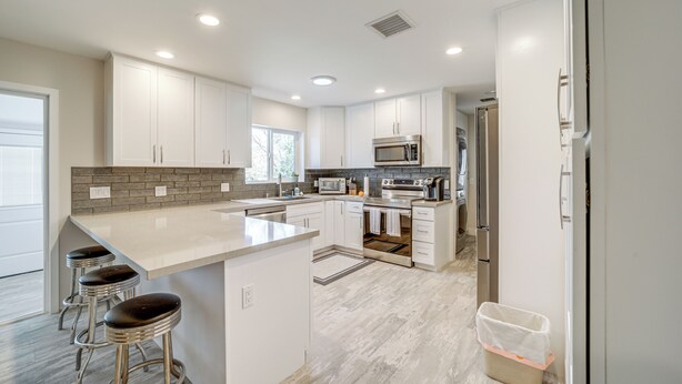 A modern kitchen with white cabinets, a large island with stools, stainless steel appliances, and a view to the outside.