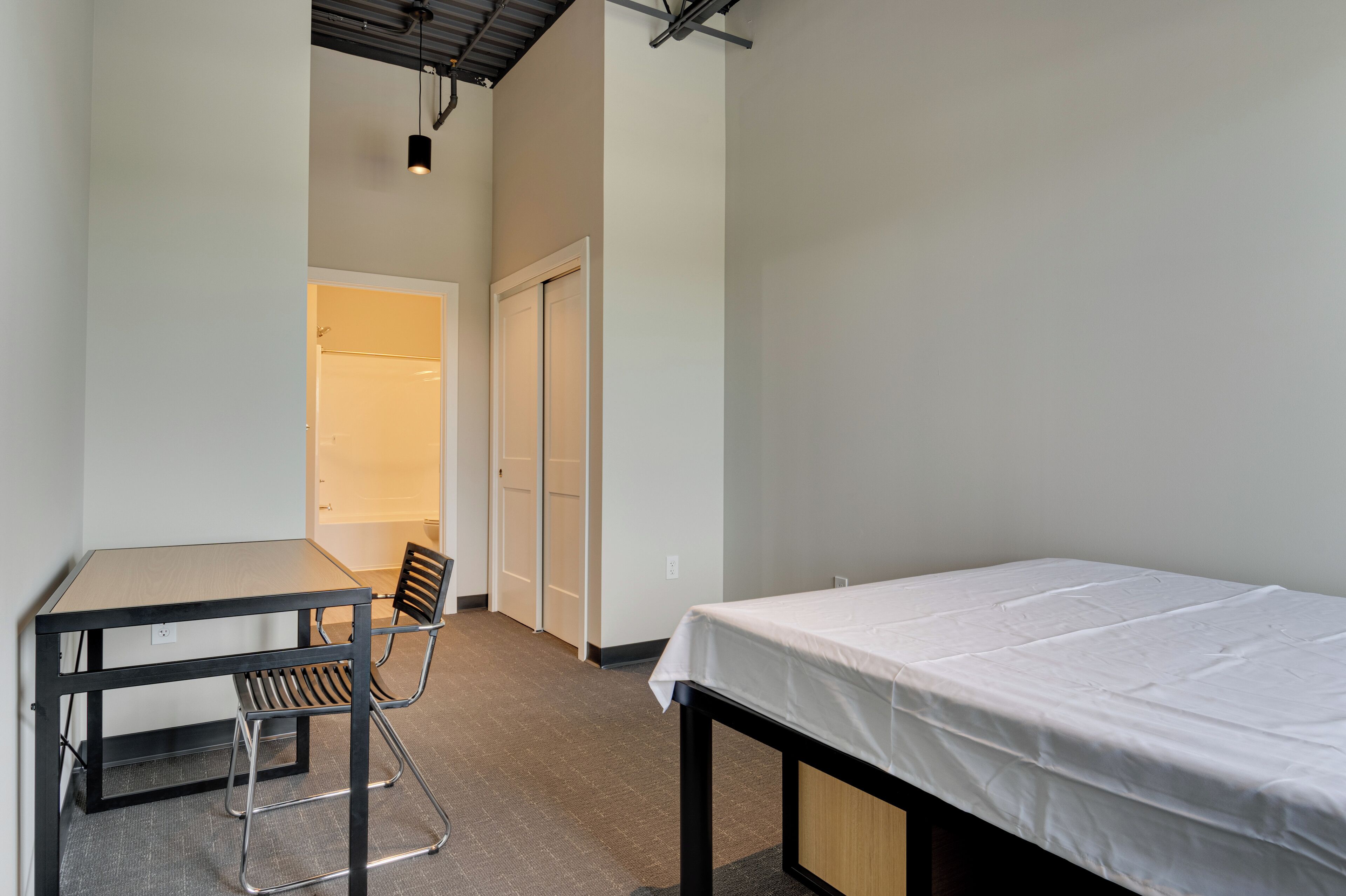 Une petite pièce bien éclairée, avec un lit simple, une table et une chaise.