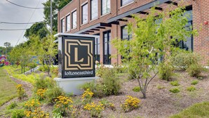 A building with a sign reading "loftoneastthird" surrounded by a landscaped garden with yellow flowers.