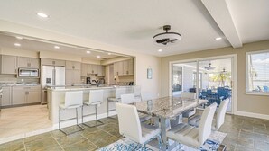 A modern kitchen with a central island, white bar stools, and a dining area with a marble table. - Boat Dock & Pool: Bayfront Crystal River Home (Crystal River)