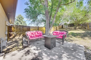 Un patio con dos sillas rosadas acolchadas y una mesa, rodeado por una valla de madera y árboles.