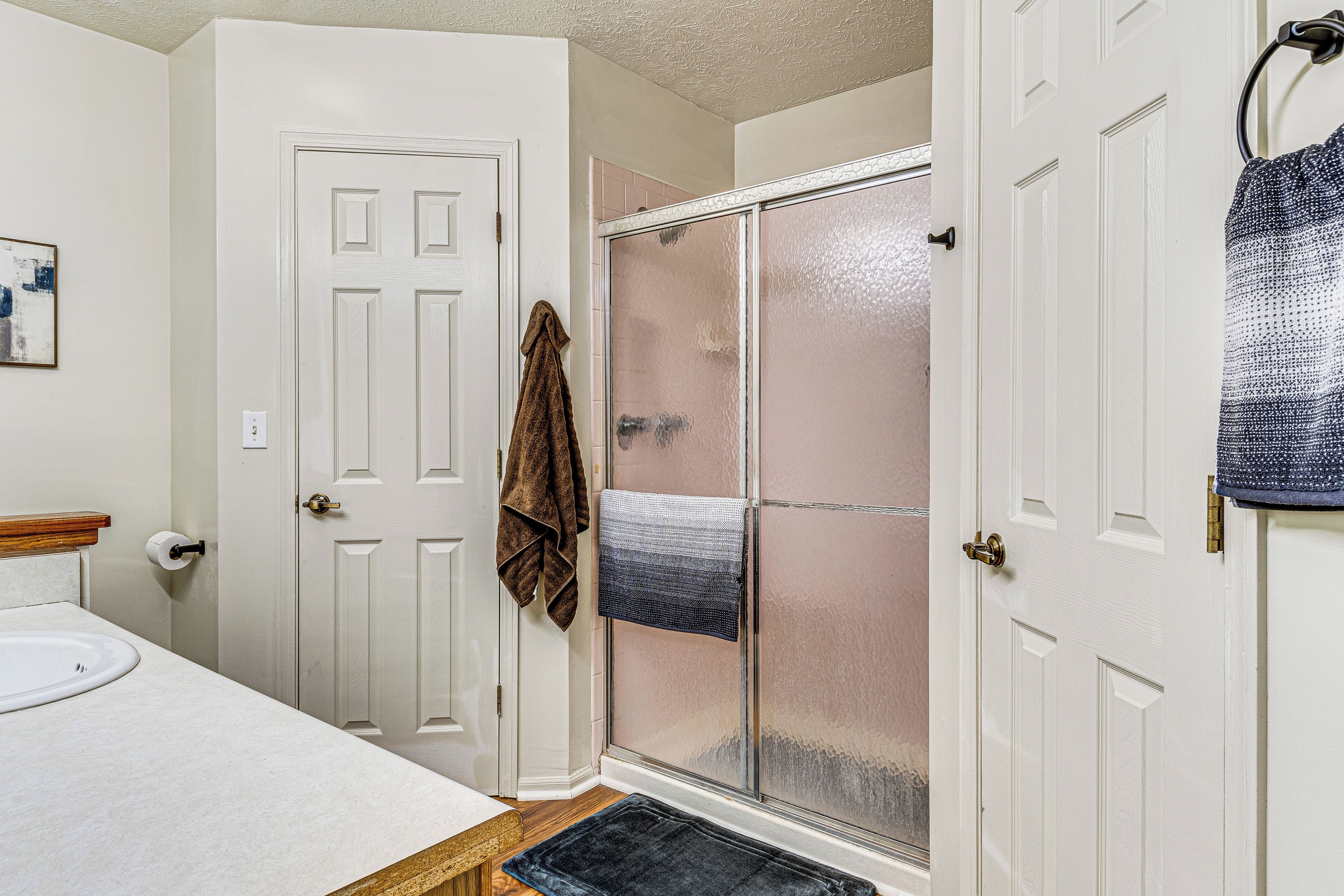 A bathroom with a white sink, a shower with a glass door, and a towel hanging on the door.