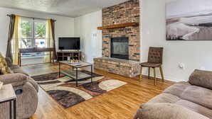 A living room with a brick fireplace, wooden flooring, and a large painting on the wall. - 14 Mi to Lucas Oil Stadium: Fire Pit & Grill! (Indianapolis)
