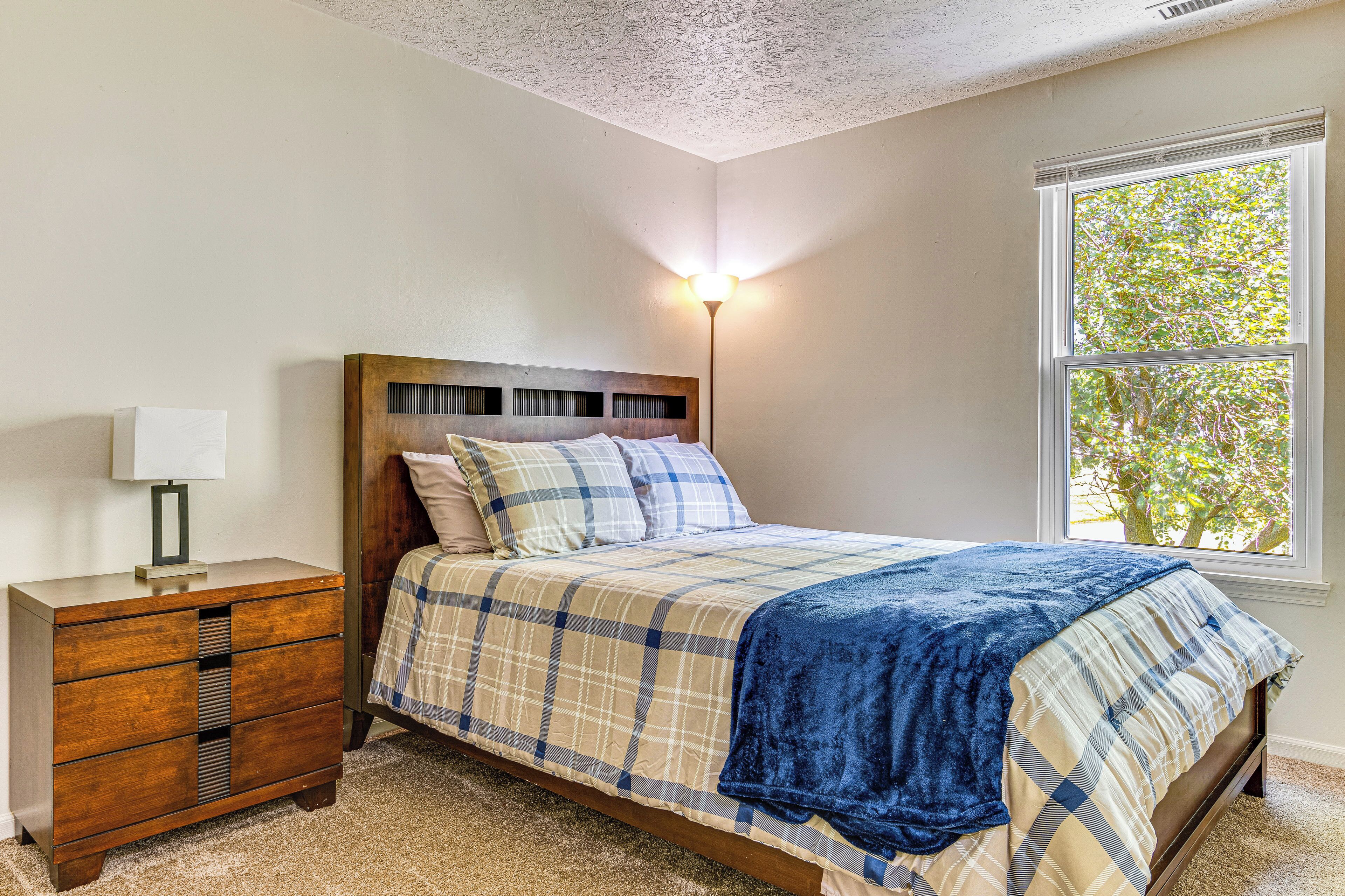 A bedroom with a bed, a nightstand, a lamp, and a window with a view of trees.