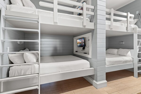 A bunk bed room with white bedding and a mounted TV.