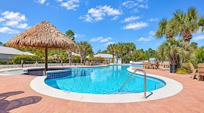 A swimming pool with a thatched roof structure, surrounded by palm trees and lounge chairs. - Sandy Pines Cottage | Private 3BR, 2 Pools + Beach Nearby (Gulf Shores)