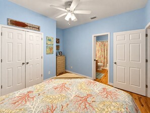 A bedroom with a bed, a ceiling fan, a dresser, and a bathroom visible through an open door. - Sandy Pines Cottage | Private 3BR, 2 Pools + Beach Nearby (Gulf Shores)