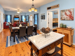 A spacious living area with a dining table, chairs, a kitchen area, and a cozy seating area with a red sofa. - Sandy Pines Cottage | Private 3BR, 2 Pools + Beach Nearby (Gulf Shores)