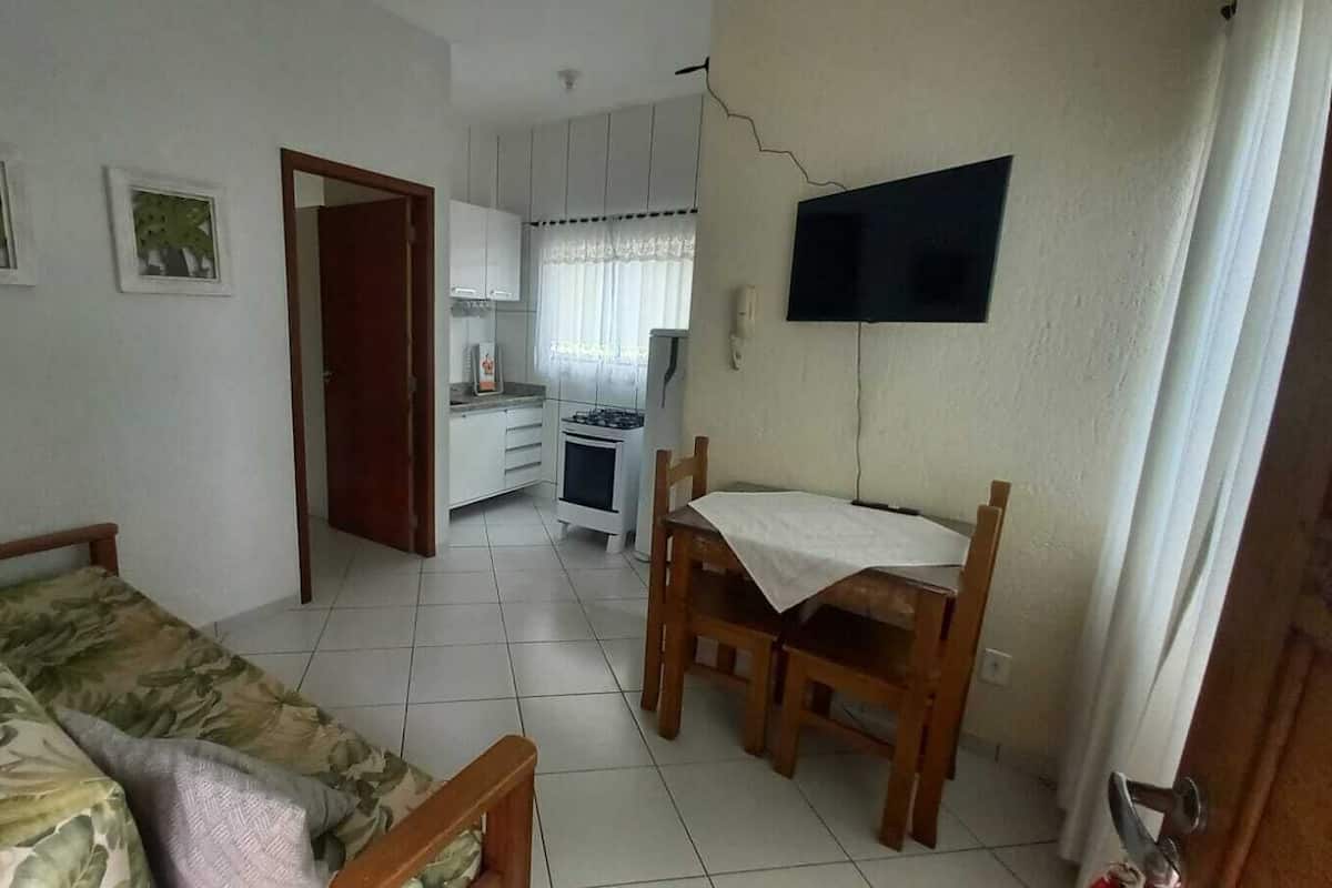 Een gezellig en compact leefruimte met een bank, een eettafel met stoelen, een keukenhoek en een aan de muur bevestigde televisie.