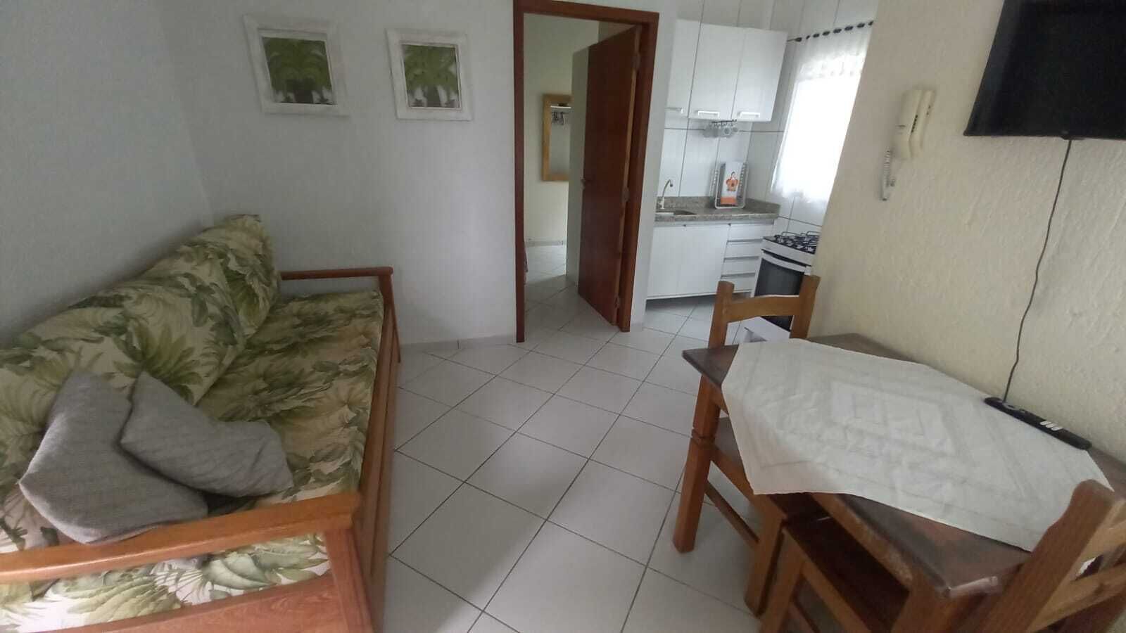 Um espaço de estar pequeno e integrado, com sofá, mesa de jantar e cozinha.