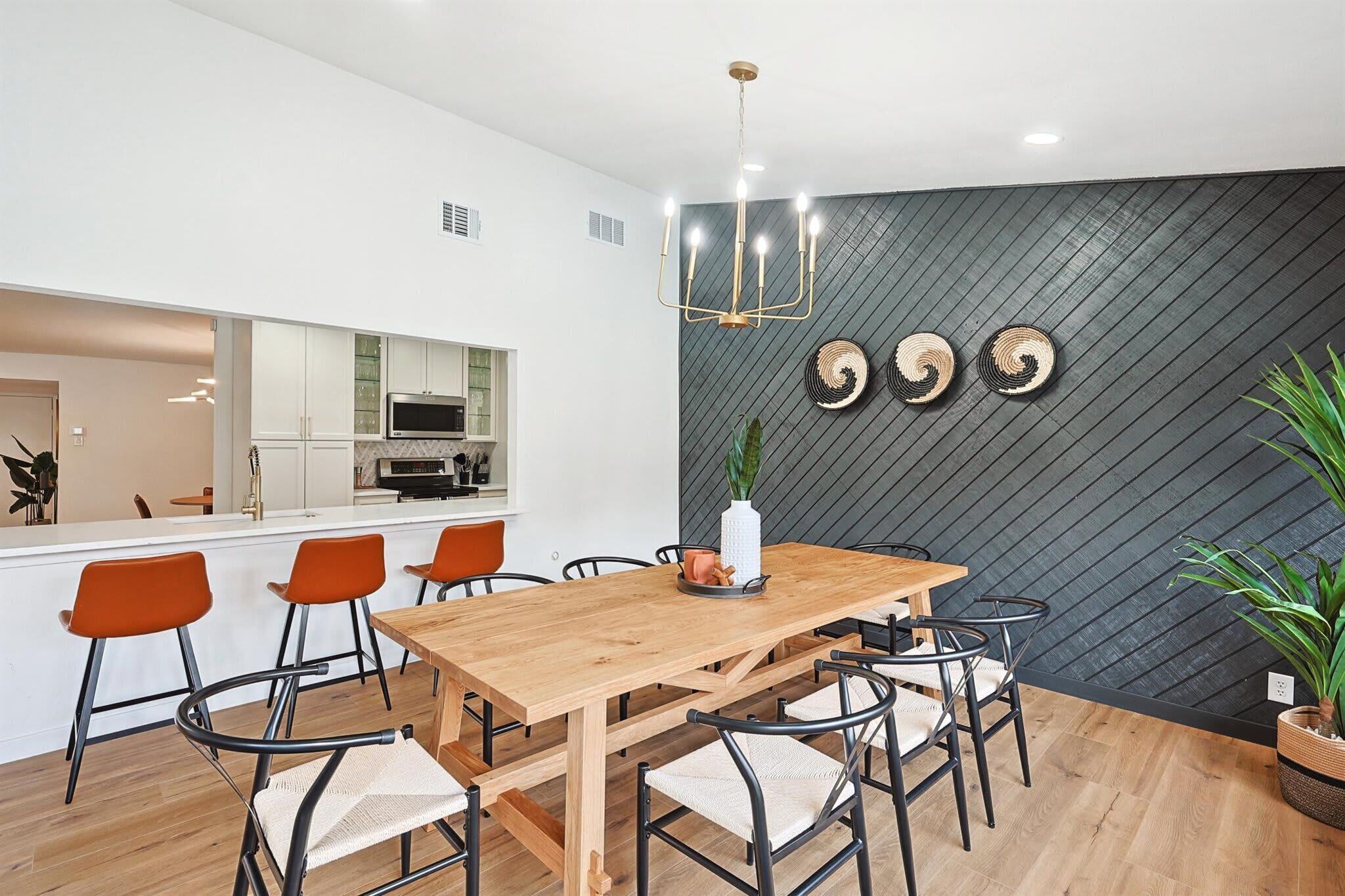 Un comedor moderno con una mesa de madera, sillas anaranjadas y una pared negra con textura.