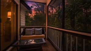 A balcony with a cushioned seating area, a glass table, and a view of trees and sky.