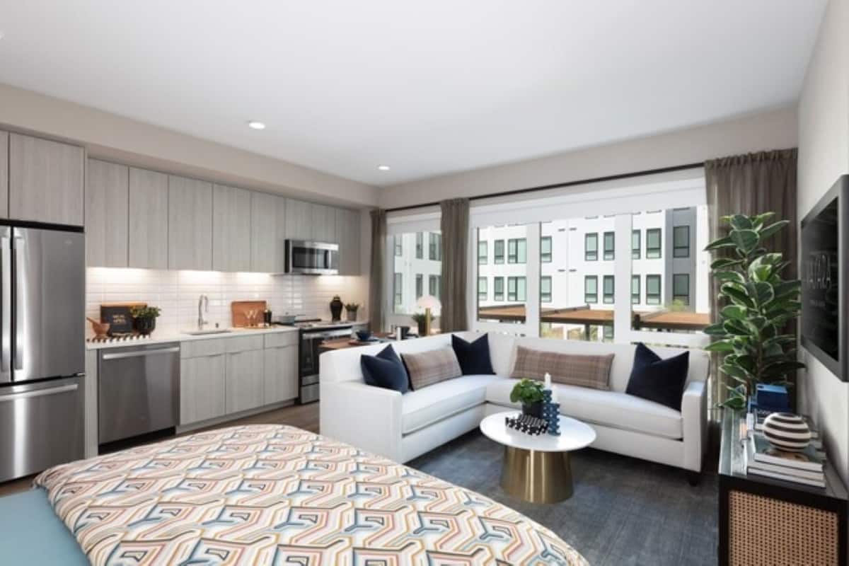 A modern apartment with a kitchen, a living area with a sofa and coffee table, and large windows with a city view.
