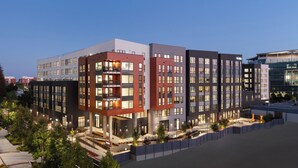 Un immeuble moderne à plusieurs étages, comprenant des logements et des espaces commerciaux, doté de balcons et de grandes fenêtres.