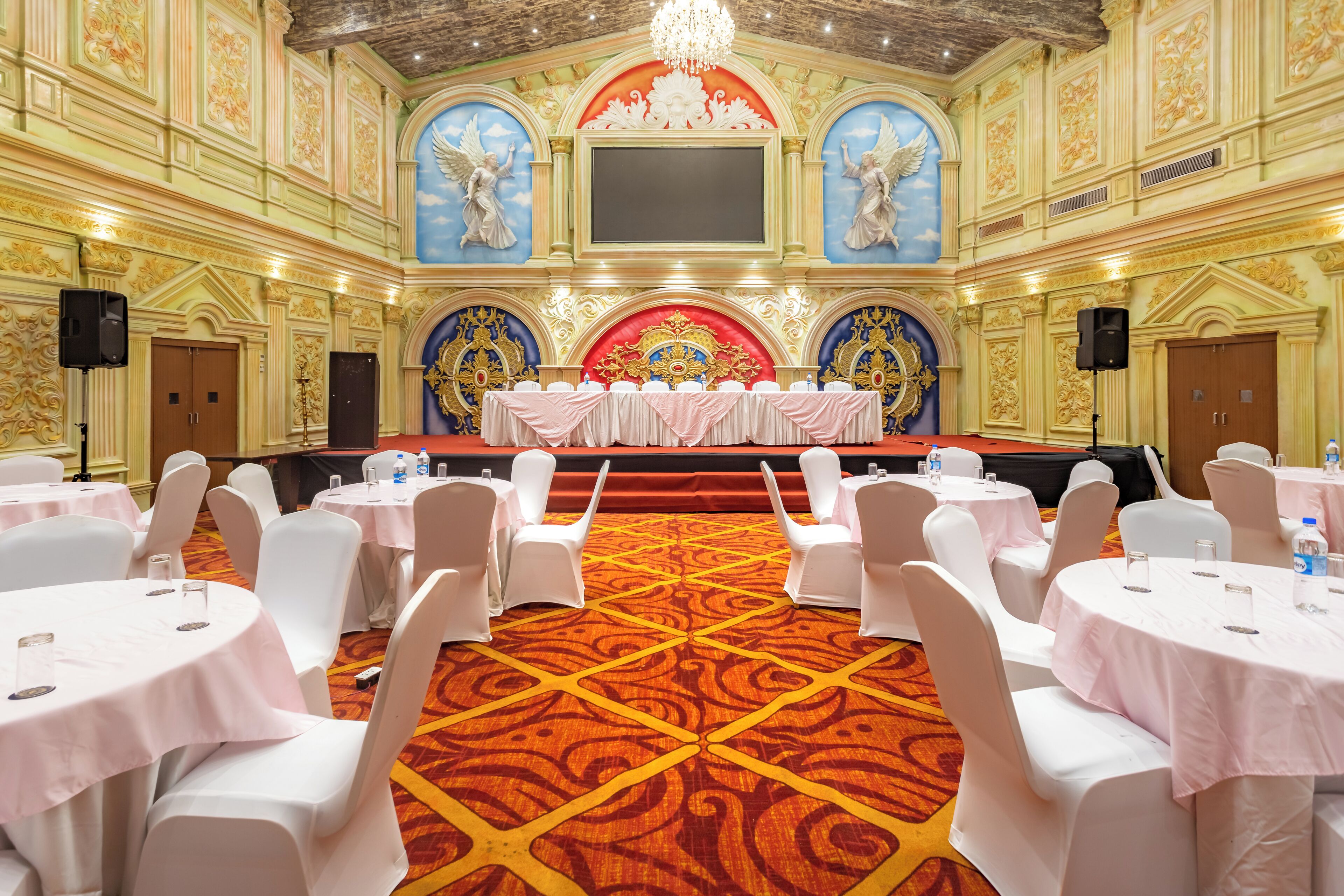 A banquet hall with round tables, white chairs, and a stage with a red backdrop.