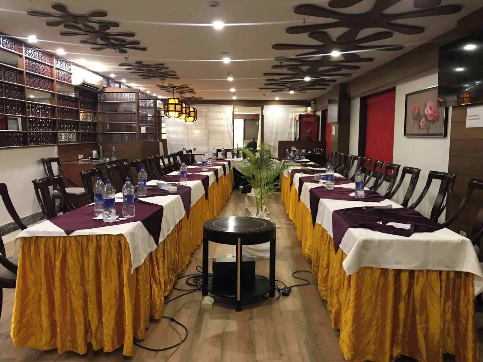 A conference room with long tables, chairs, and a large plant in the center.