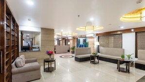 Un amplio vestíbulo con sofá, sillones y una mesa de centro, con un diseño moderno y detalles de madera, además de un espejo grande.