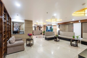 Un amplio vestíbulo con sofá, sillones y una mesa de centro, con un diseño moderno y detalles de madera, además de un espejo grande.