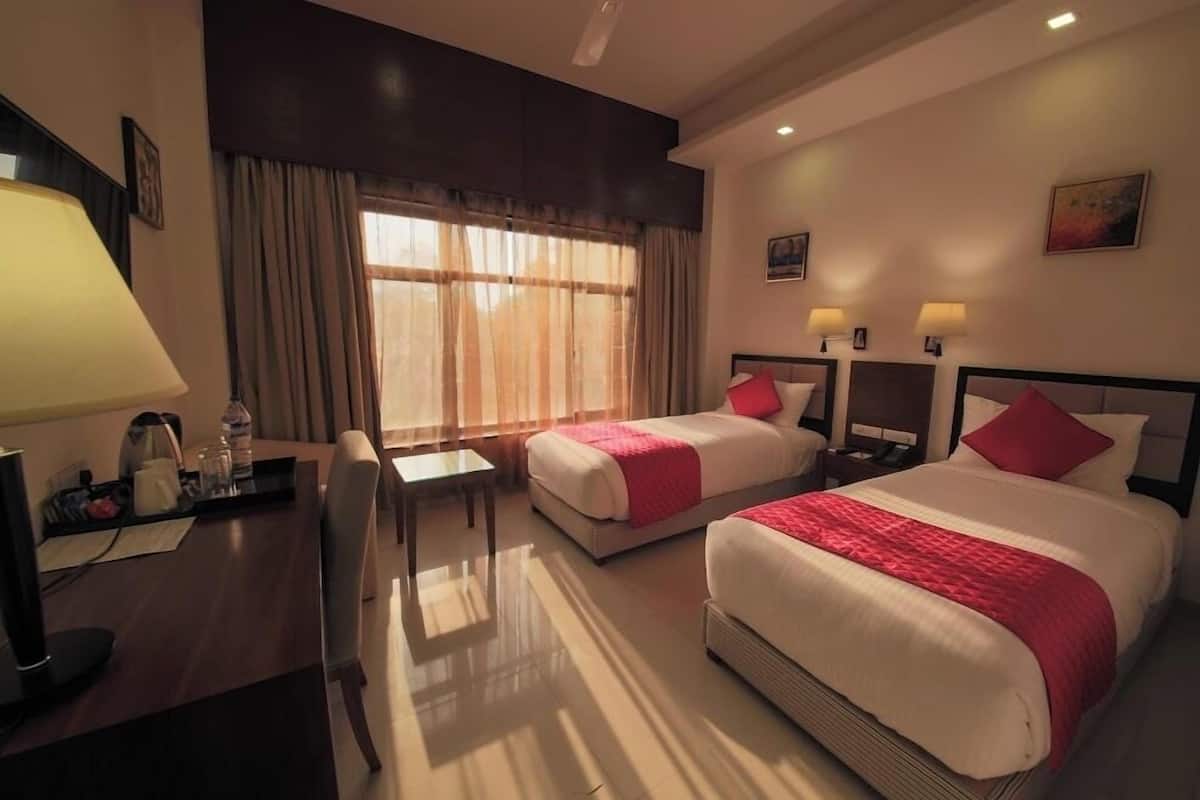 A hotel room with two beds, a desk, a chair, and a window with curtains.