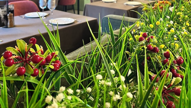 A restaurant with wooden ceiling beams, tables set for dining, and a variety of flowers in the foreground. - Skala (Burabay)