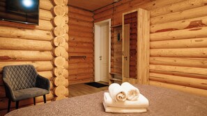 A log cabin room with a quilted chair, a table with towels, and a wooden door. - Skala (Burabay)