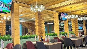 Un restaurante con vigas de madera en el techo, lámparas colgantes y varias pantallas de televisión. Las mesas están dispuestas con sillas y vajilla.