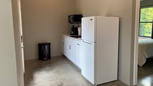 A compact kitchen with white cabinets, a white refrigerator, a black microwave, and a trash bin. - Lovely 2-bedroom cottage located in downtown Mount Vernon! (Mount Vernon)