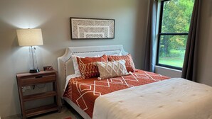 A neatly arranged bedroom with a bed, a bedside table, a lamp, and a window with a view of greenery. - Lovely 2-bedroom cottage located in downtown Mount Vernon! (Mount Vernon)