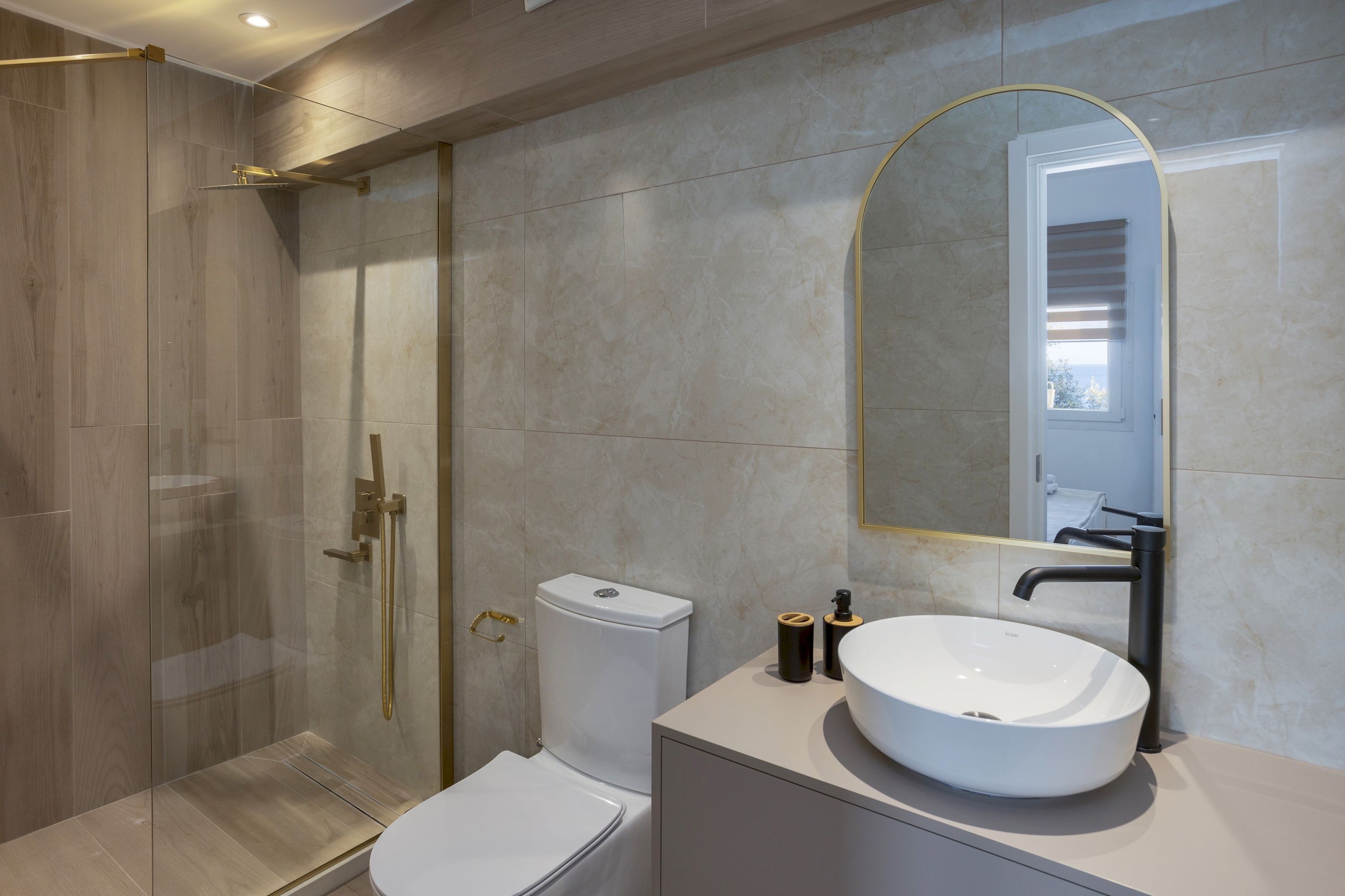 A modern bathroom with a glass-enclosed shower, a white toilet, and a large sink with a mirror above it.