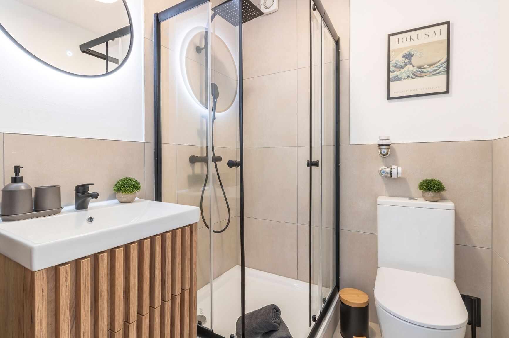 A modern bathroom with a glass-enclosed shower, a wooden vanity, a toilet, and a wall-mounted sink.