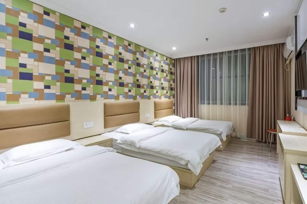 Habitación de hotel con tres camas, un escritorio, televisor montado en la pared y ventana con cortinas.
