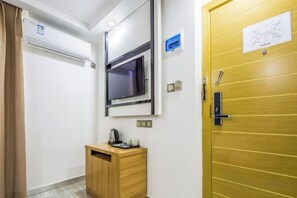 A hotel room with a wooden door, a small wooden cabinet, a wall-mounted TV, and a window. - Shenghao Hotel (Guangzhou Railway Station) (Guangzhou)