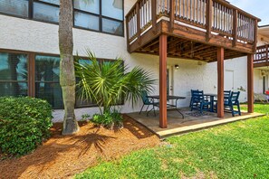A covered outdoor patio with a table and chairs, a small garden with a palm tree, and a building with windows and a door.