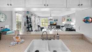 A kitchen with white cabinets, a double sink, and a countertop with kitchen items. - 🌊Beachview 107-🐾Pet Friendly🐾-2BR-Close To The Beach🌊 (Navarre Beach)