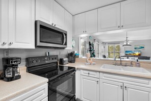 A modern kitchen with white cabinets, a built-in microwave, a stove, and a sink. - 🌊Beachview 107-🐾Pet Friendly🐾-2BR-Close To The Beach🌊 (Navarre Beach)