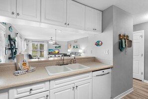A modern kitchen with white cabinets, a double sink, and a countertop with a dish rack and a bag of chips. - 🌊Beachview 107-🐾Pet Friendly🐾-2BR-Close To The Beach🌊 (Navarre Beach)