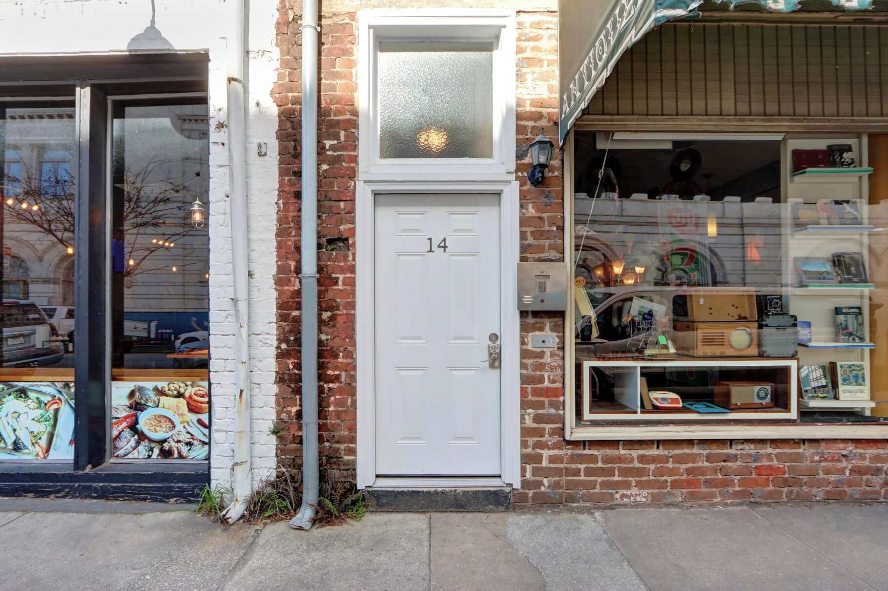 A storefront with a white door marked with the number 14, a brick wall, and a display window with various items.