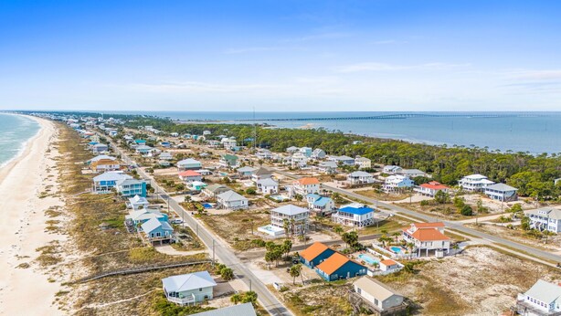 Zona residencial costera con casas a lo largo de la playa, vista despejada del océano y un puente en la distancia.