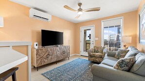 A living room with a flat-screen TV, a ceiling fan, a patterned rug, and a sofa with decorative pillows. - Sunflower 3, Pet friendly, Beachfront. (Eastpoint)
