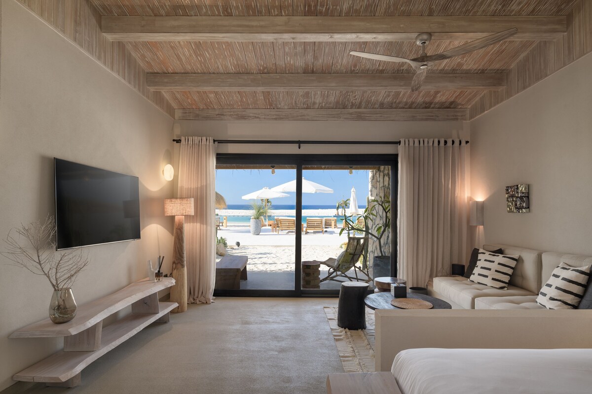 Een moderne hotelkamer met een grote televisie, een bank, een salontafel en uitzicht op het strand.