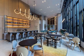 A modern bar area with a long counter, multiple stools, and tables. There are large windows on one side and a seating area with round tables and chairs. - YOTEL Tokyo Ginza (Tokyo)