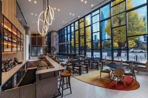 A modern bar area with a bar counter, stools, and seating. Large windows provide a view of the outside. - YOTEL Tokyo Ginza (Tokyo)