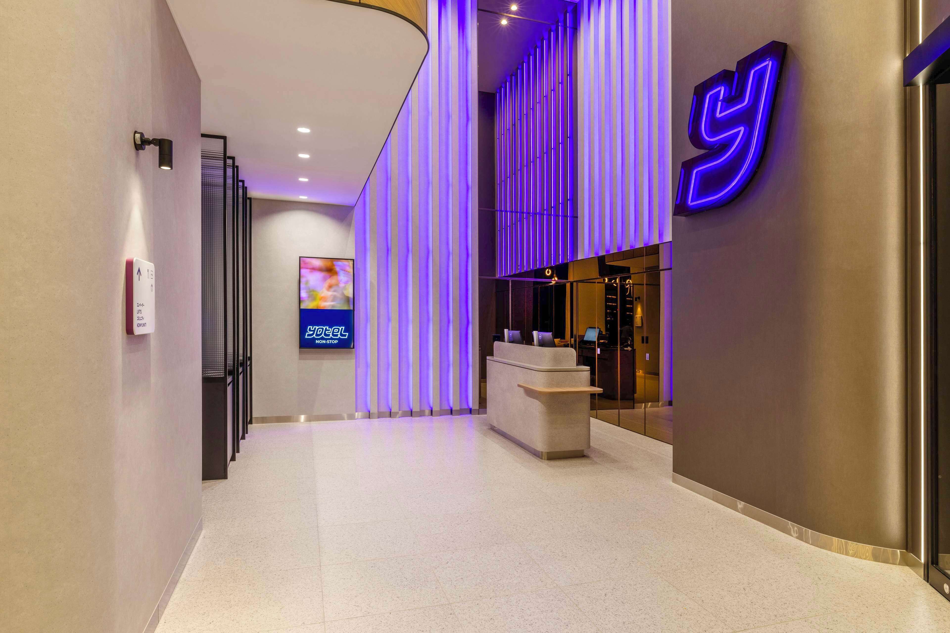 A modern hotel lobby with a reception desk, a large digital screen, and a distinctive neon sign.
