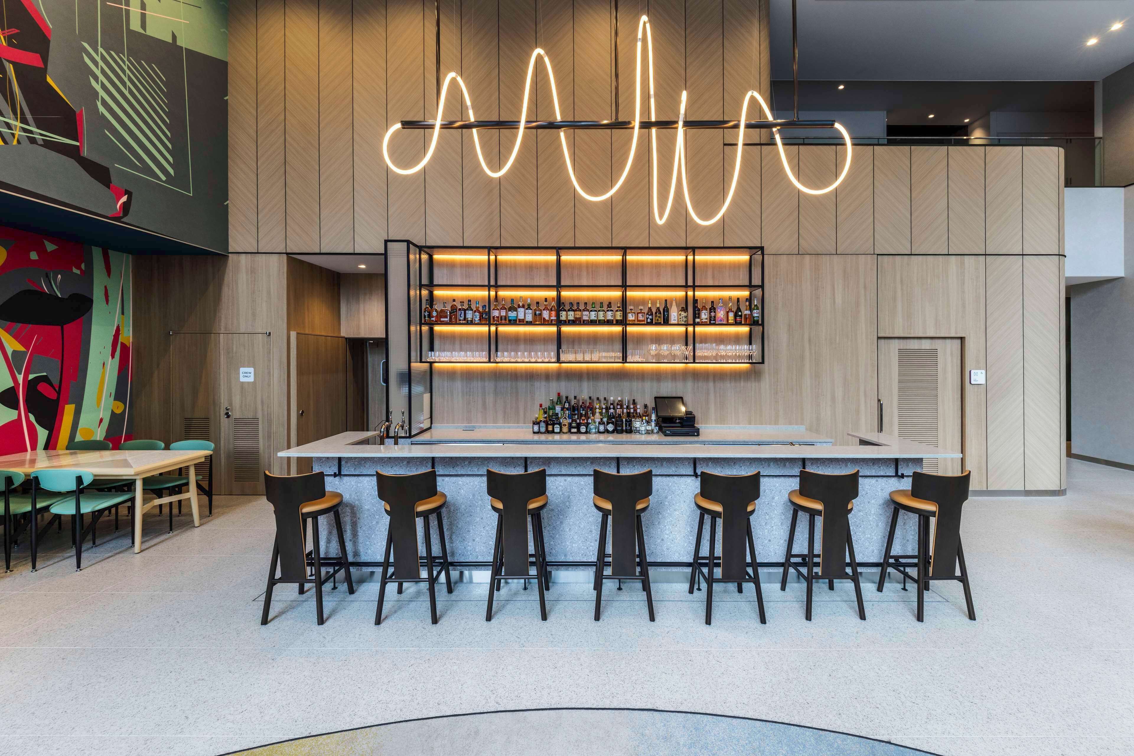 A modern bar area with a central island, bar stools, and a variety of bottles.