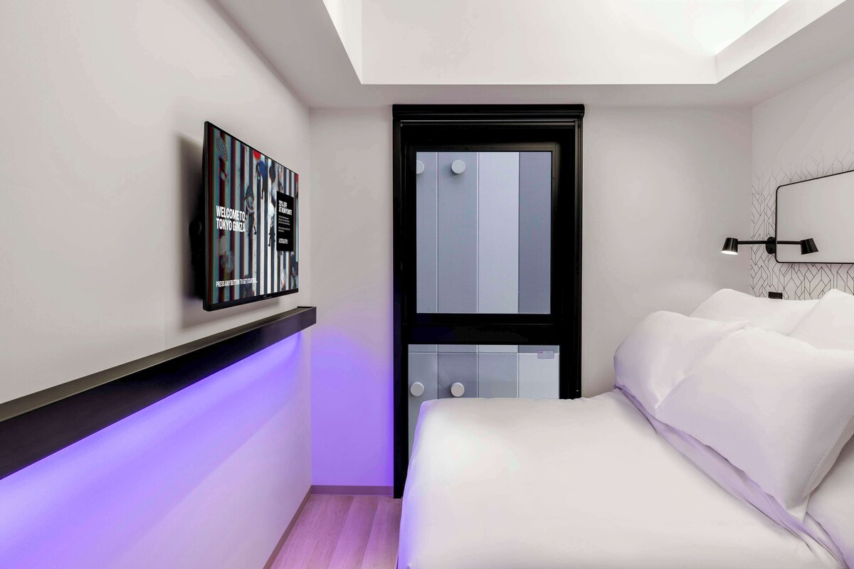 A modern bedroom with a bed, a wall-mounted TV, and a skylight.